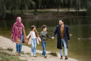 Parkta göl kenarında gezen mutlu Arap ailesi 