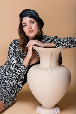 Bej rengi vazonun yanında poz veren zebra desenli ve siyah bereli bir model. 