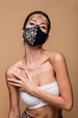 Kaplan makyajlı kadın ve hayvan desenli koruyucu maske bej üzerine izole edilmiş poz veriyor.