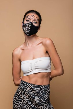 Kaplan makyajlı ve hayvan desenli koruyucu maskeli bir model bej üzerine izole edilmiş.
