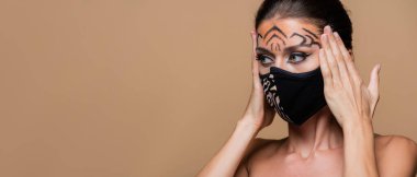 Kaplan makyajlı ve hayvan desenli koruyucu maskeli bir model bej ve pankartta izole bir şekilde duruyor.