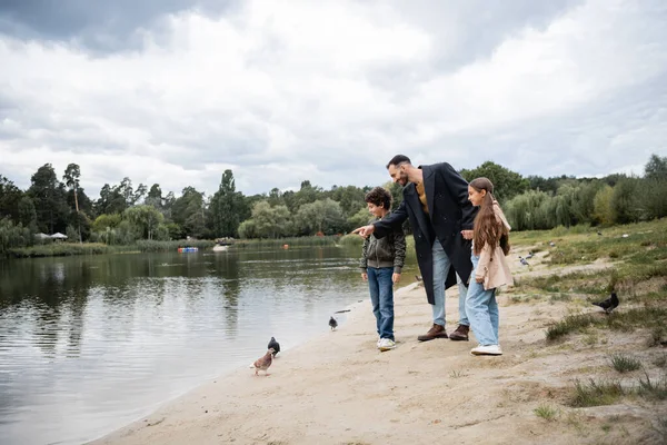 Arabian kids standing near father pointing at lake in park