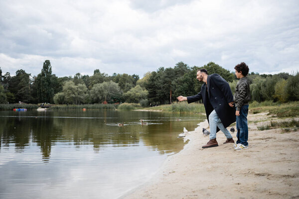 Side view of muslim father standing near son and lake in park