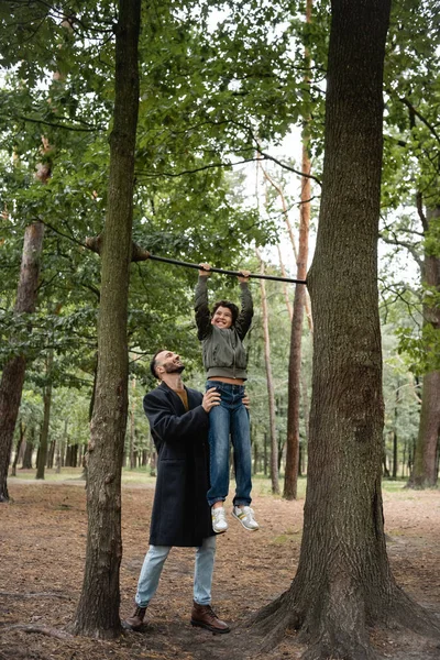 Sonriente Padre Árabe Sosteniendo Hijo Cerca Barra Horizontal Árboles — Foto de Stock