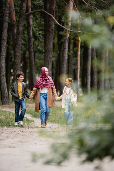 Cheerful arabian mother in hijab walking with kids in park 