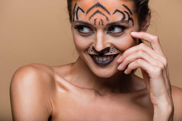 joyful young woman with bare shoulders and tiger makeup posing isolated on beige