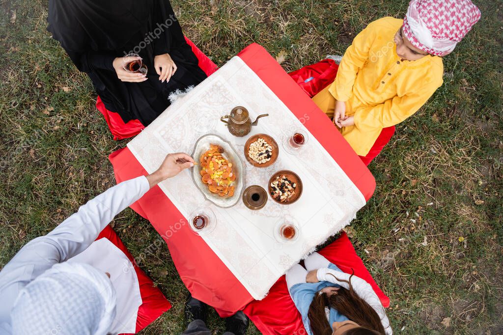 Top view of muslim family sitting near tea and food in park 