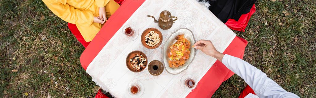 Top view of man and boy sitting near traditional arabian tea and food in park, banner 