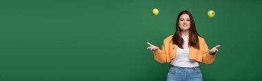 Cheerful woman with overweight throwing apples isolated on green, banner  clipart