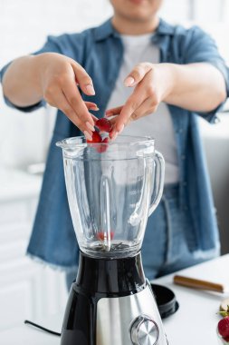 Mutfaktaki blender 'a çilek koyan bulanık, iri yarı kadının görüntüsü. 
