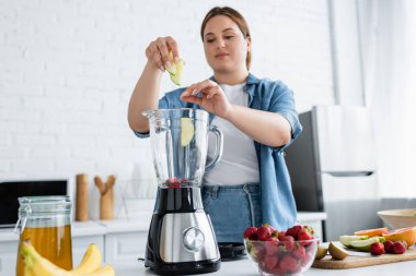 Blurred woman with overweight cooking smoothie in blender in kitchen  clipart