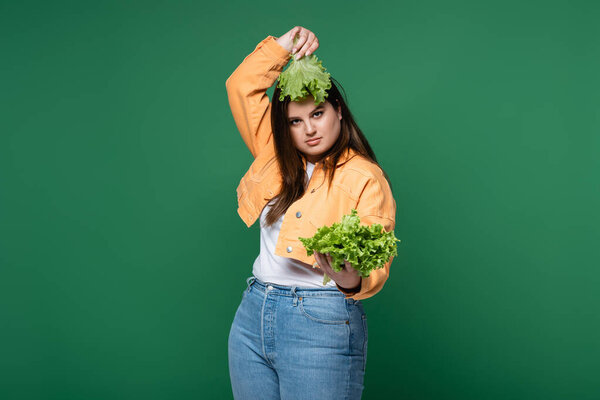 Молодая женщина с избыточным весом держит салат возле головы изолированы на зеленый 