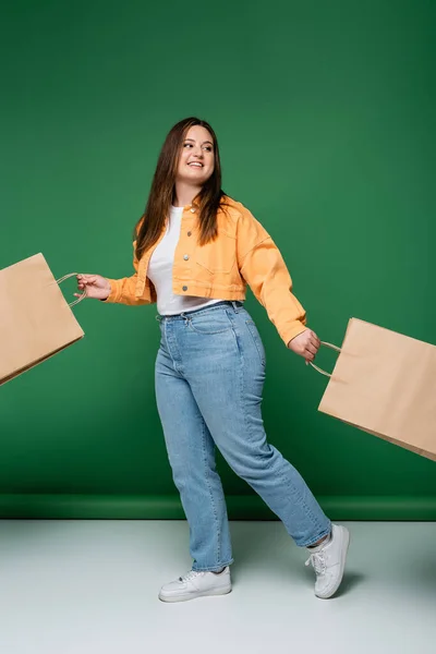 Cheerful body positive woman with craft shopping bags walking on green background