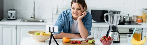 ポジティブな女性とともに太りすぎ見てスマートフォン近く果物上のキッチンテーブル バナー — ストック写真