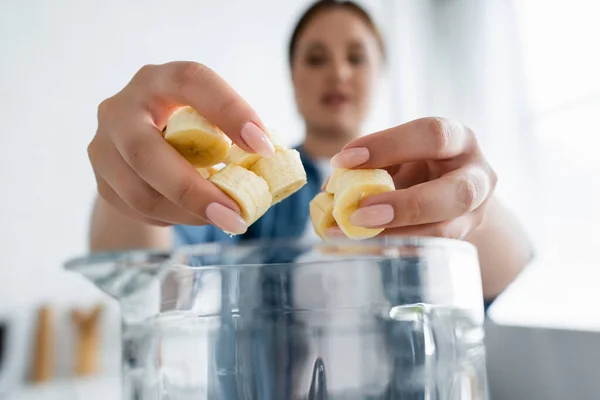 台所でミキサーの近くにスライスバナナを保持している若い女性 — ストック写真