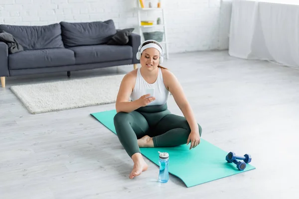 Sonriente Deportista Tamaño Grande Con Auriculares Usando Smartphone Colchoneta Fitness — Foto de Stock