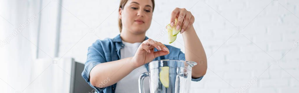 Blurred woman with overweight putting apple slices in blender in kitchen, banner 
