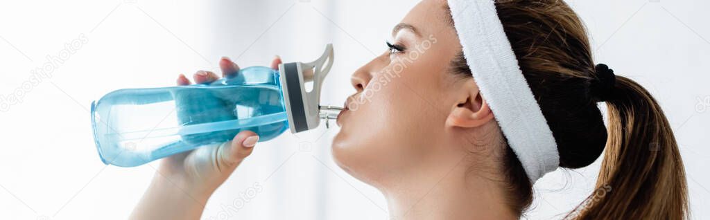 Young sportswoman in headband drinking water from sports bottle at home, banner 