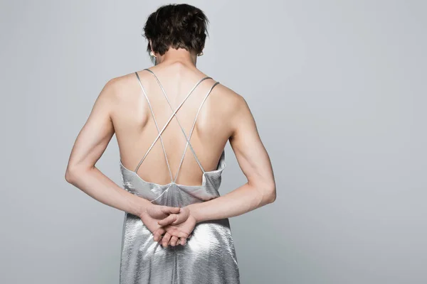 back view of transsexual man in slip dress standing with hands behind back isolated on gray