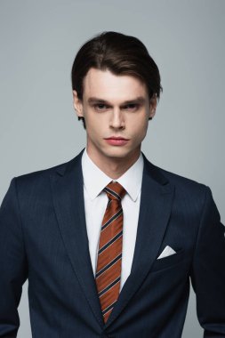 Takım elbiseli genç işadamı gri kameraya bakıyor.