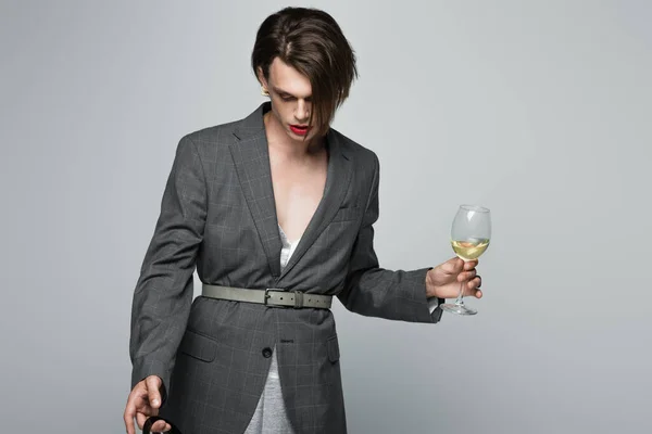 young transgender man in blazer holding glass of wine isolated on grey