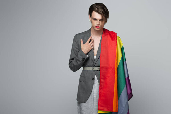 молодой транссексуал в блейзере и платье с флагом lgbt, изолированным на сером