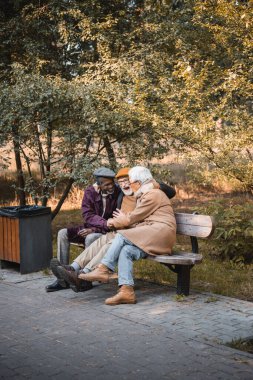 Mutlu çok ırklı son sınıf öğrencileri parkta yedek kulübesinde vakit geçiriyor. 