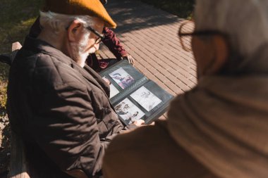Senor man holding photo album near multiethnic friends in park  clipart