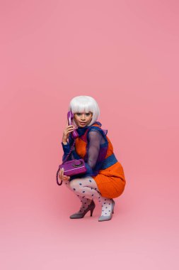 Gülümseyen Asyalı pop sanat modeli pembe arka planda telefonla konuşurken kameraya bakıyor.