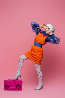 Beyaz peruklu Asyalı pop sanat modeli pembe arka planda müzik kutusunun yanında poz veriyor
