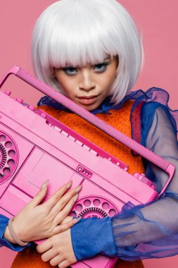 Beyaz peruklu şık Asyalı model. Pembe üzerine izole edilmiş retro teyp taşıyor. 
