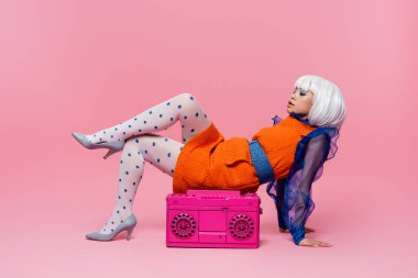 Eski moda elbiseli, beyaz peruklu şık Asyalı kadın pembe arka planda müzik kutusunun yanında poz veriyor.