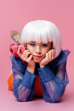 KYIV, UKRAINE - 10 Aralık 2020: Pembe arka planda yatarken beyaz peruklu Asyalı pop sanat modeli