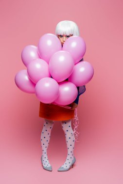 Asyalı pop sanat modeli pembe arka plandaki balonların yanındaki kameraya bakıyor.