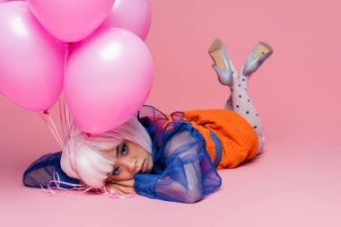 Güzel Asyalı pop sanat modeli pembe arka planda balonların yanında yatıyor.