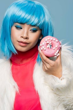 Maviye saklanmış jöleli donut yiyen Asyalı bir kadının portresi. 
