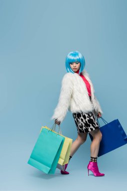 Popüler sanat tarzındaki şık Asyalı kadın mavi arka planda alışveriş torbaları tutuyor. 