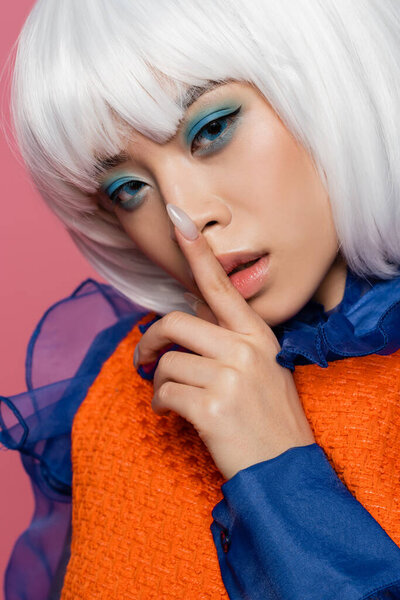 Asian model in white wig showing secret gesture isolated on pink 