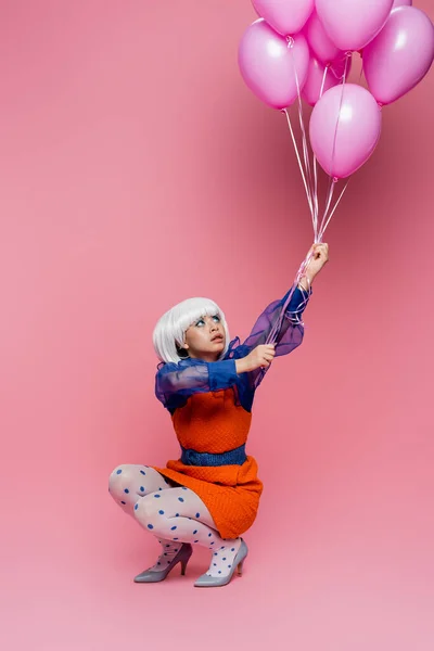 Young asian pop art model looking at balloons on pink background