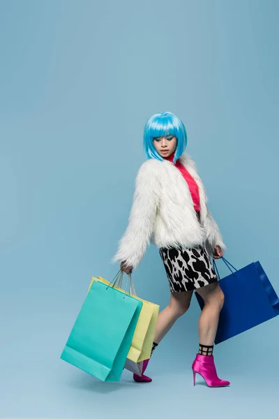 Stylish asian woman in pop art style holding shopping bags on blue background
