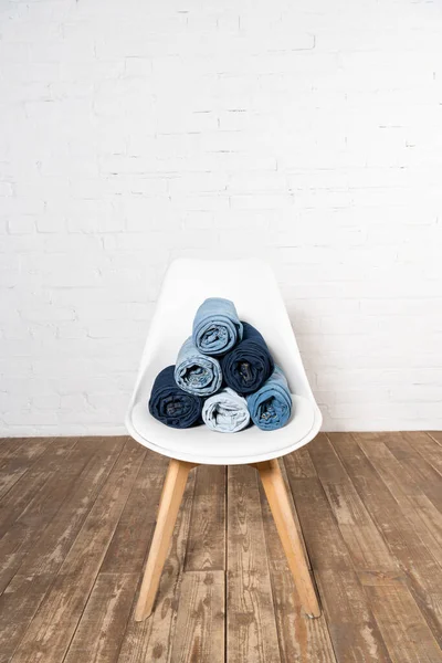 White chair with rolled denim clothing on wooden floor near brick wall — Stock Photo