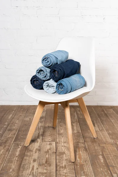 Rolled denim garments on white chair placed on wooden floor near brick wall — Stock Photo