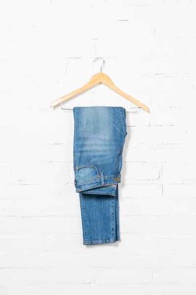 Hanger with blue jeans near white brick wall — Stock Photo