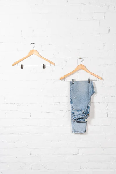 Hangers and blue jeans near white brick wall — Stock Photo