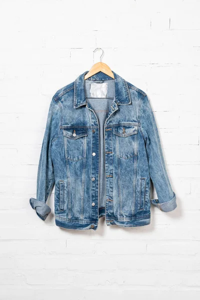 Denim jacket hanging on hanger near white brick wall — Stock Photo