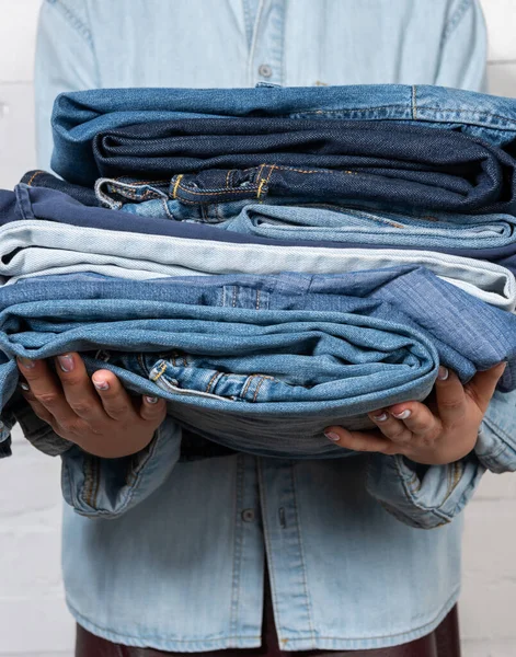 Partial view of woman holding stacked denim clothes — Stock Photo
