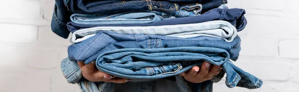 Partial view of woman with stacked denim clothes, banner — Stock Photo