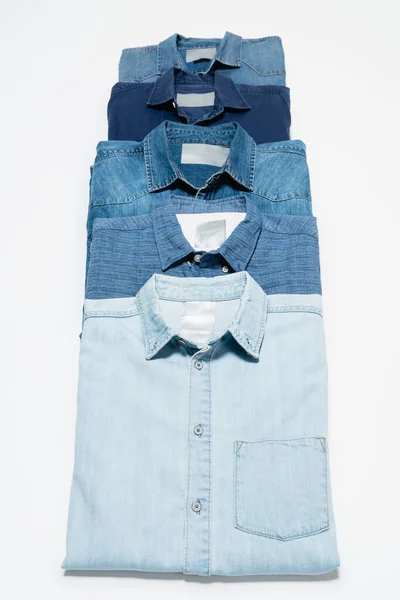Vertical row of blue denim shirts on white background, top view — Stock Photo