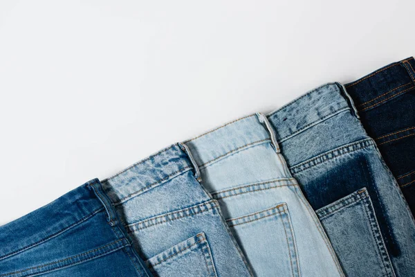 Diagonal row of various jeans on white background, top view — Stock Photo