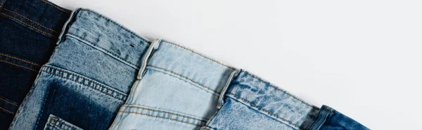 Diagonal row of different jeans on white background, top view, banner — Stock Photo